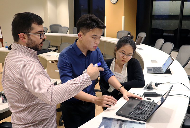 Professors instructs two students in a classroom using a laptop