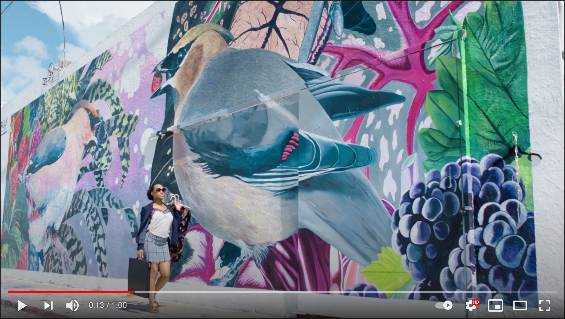 youtube video screen grab of a woman walking in front of a mural