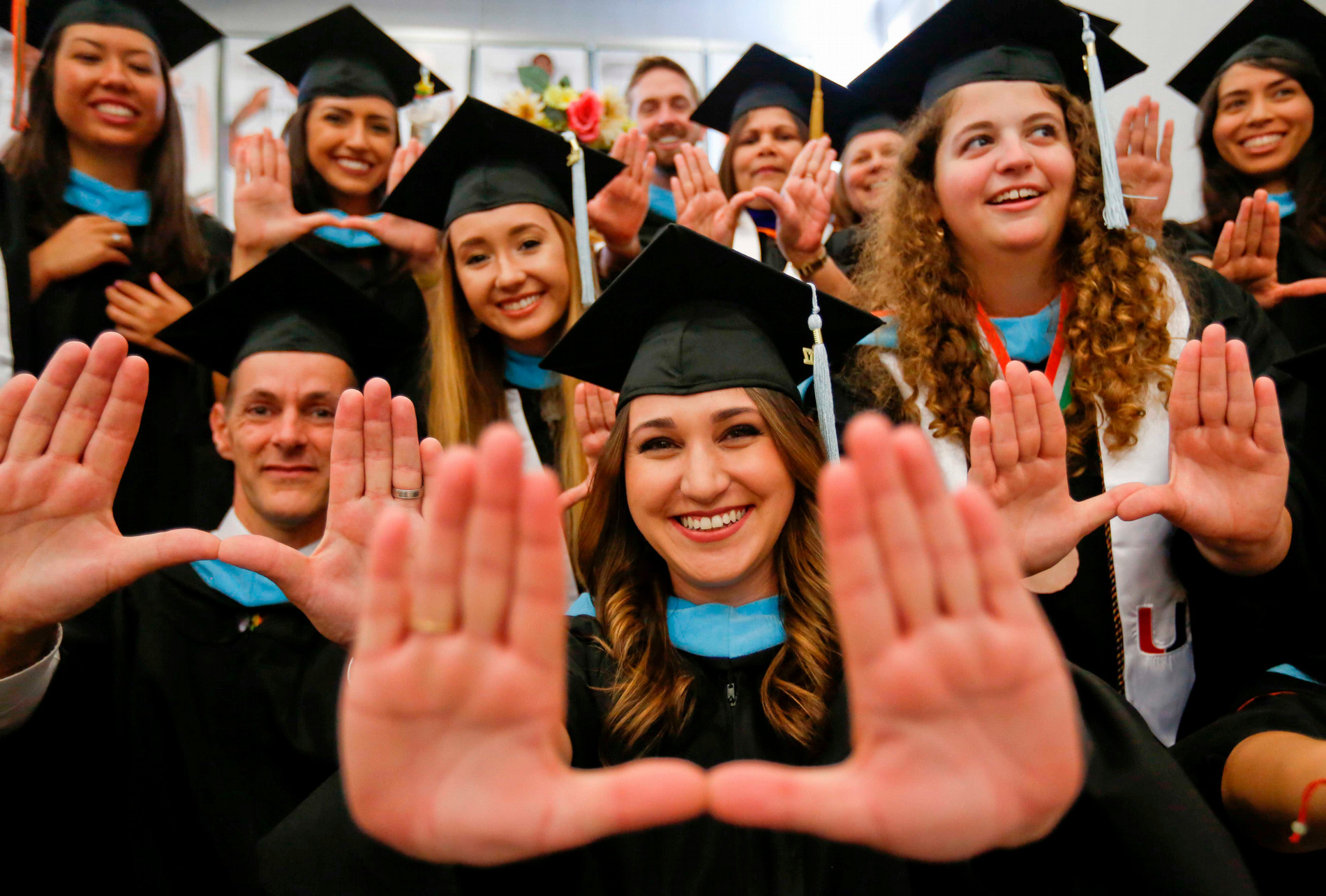 Recent graduates in ceremonial attire and mortarboards hold up the U sign with their hands.