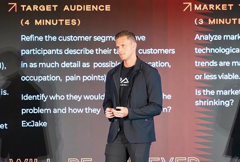 Man in black suitcoat presents the work completed on his business concept