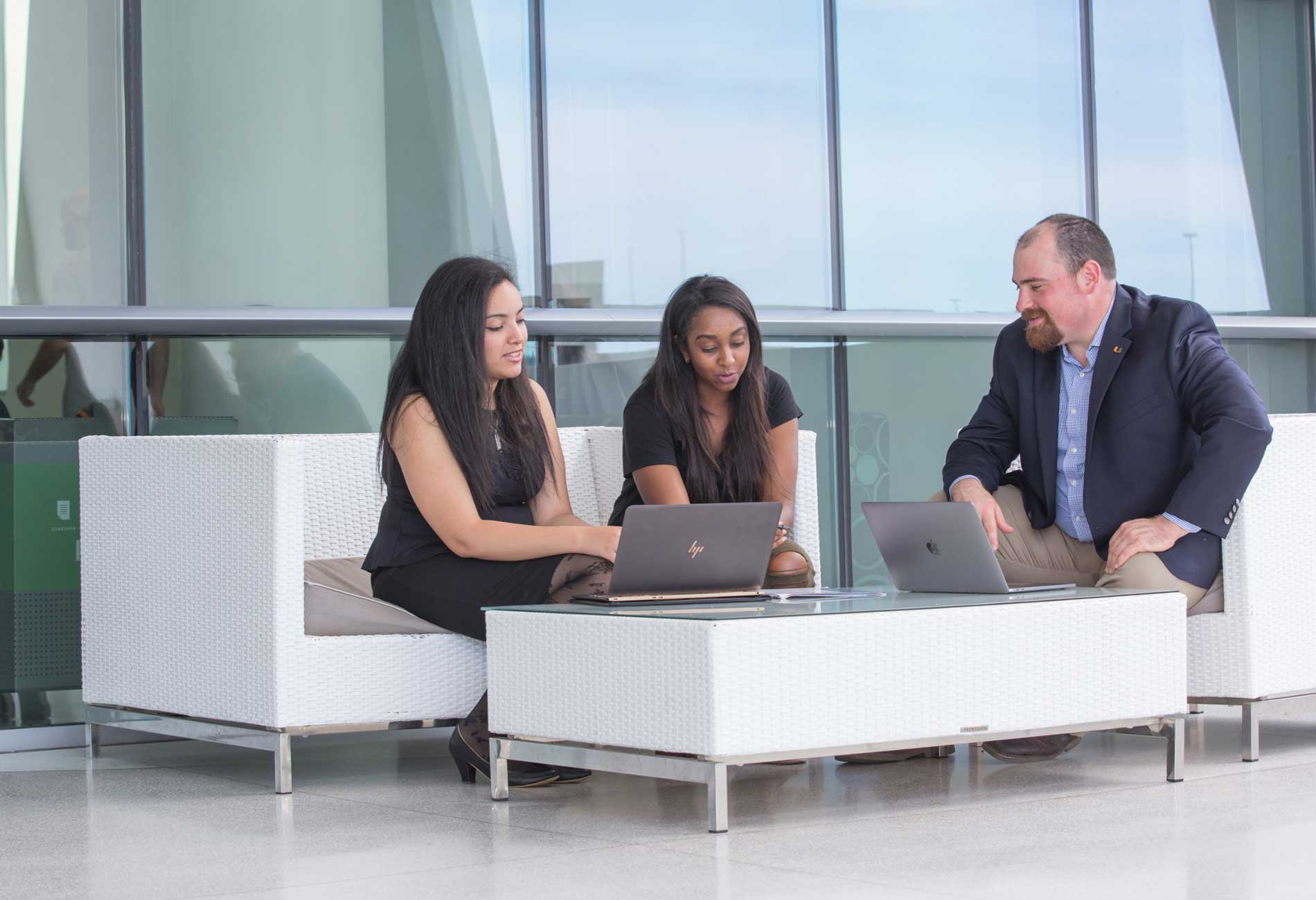 Three students work together using laptops while sitting outside