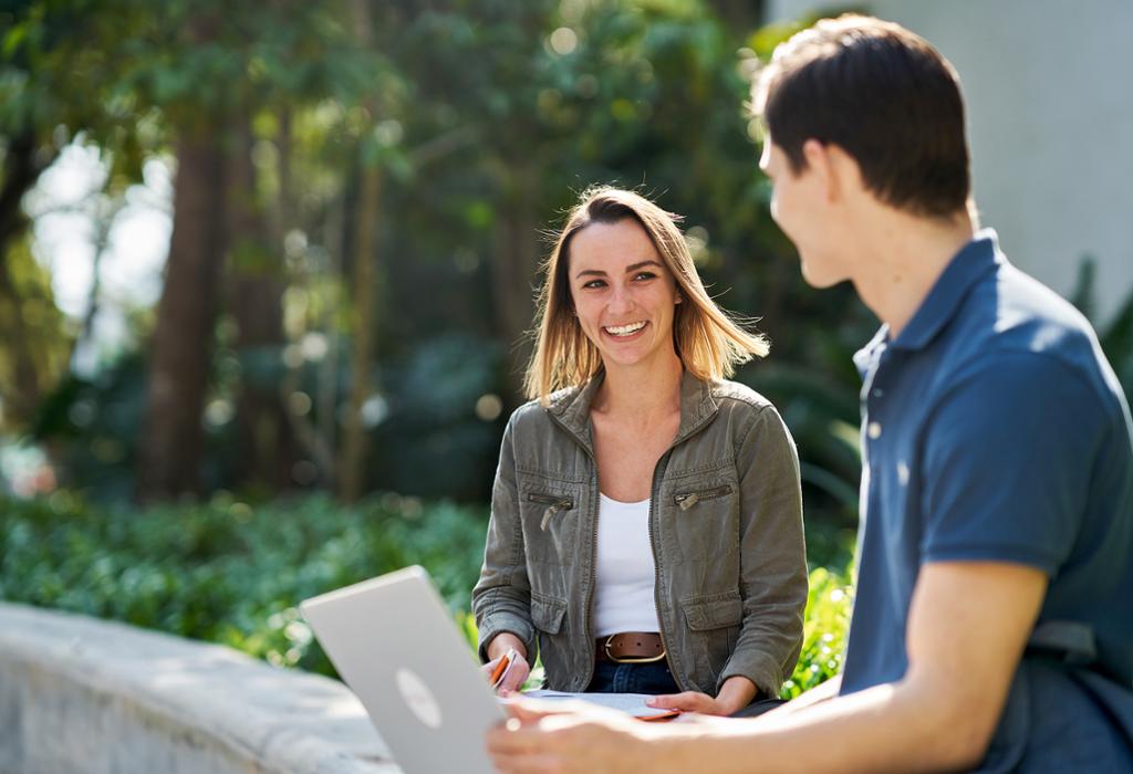 Students on laptop outdoors. Students on campus with laptop.