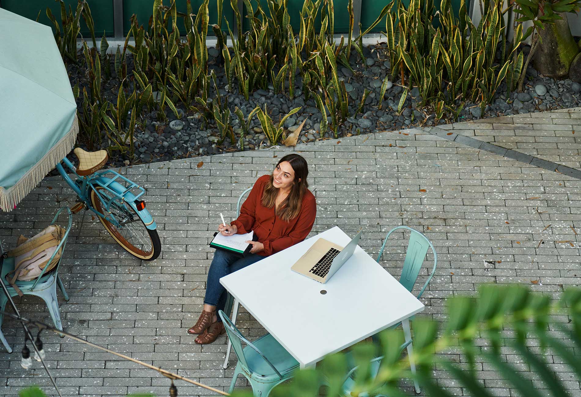 A female student looks up at the sky while sitting outside and working on a laptop