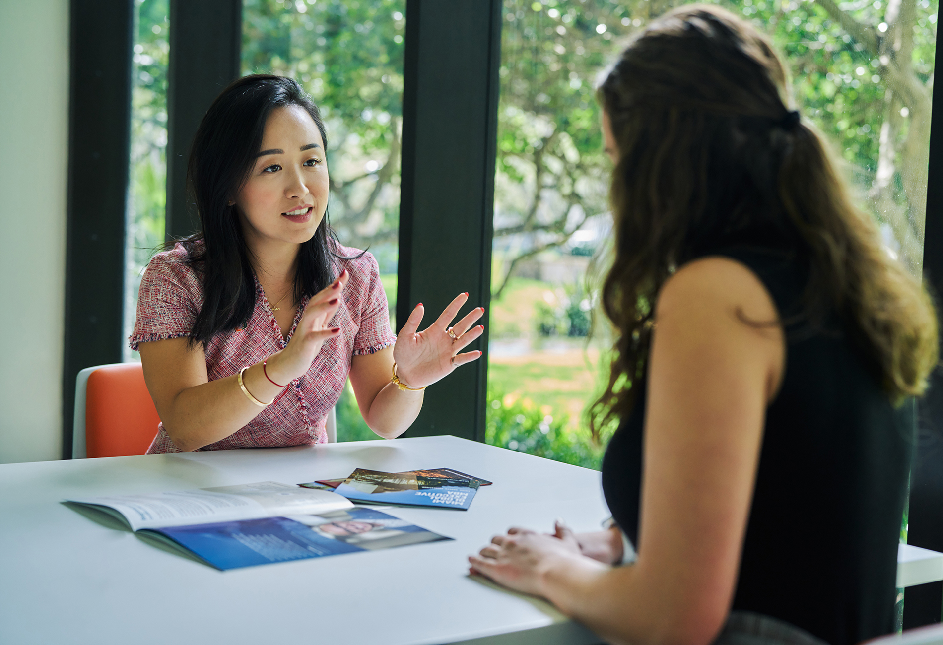 Two female students sit inside discussing programs