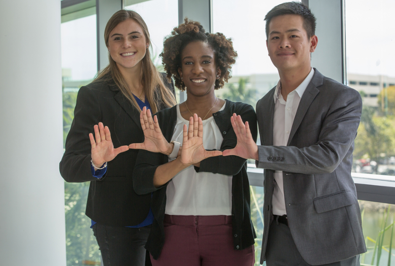 Three graduate students holding up the U sign with their hands.