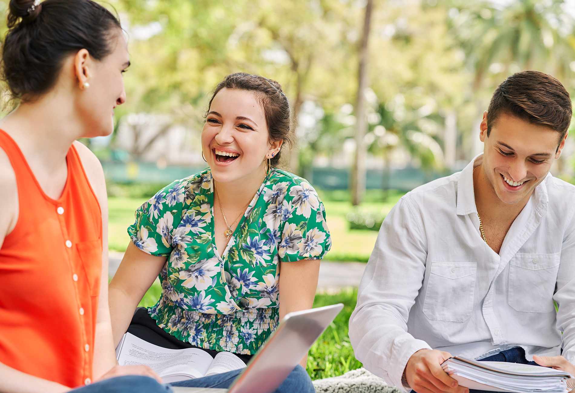 Students sitting on campus grounds. Students laughing while doing group work. Outdoor group work.