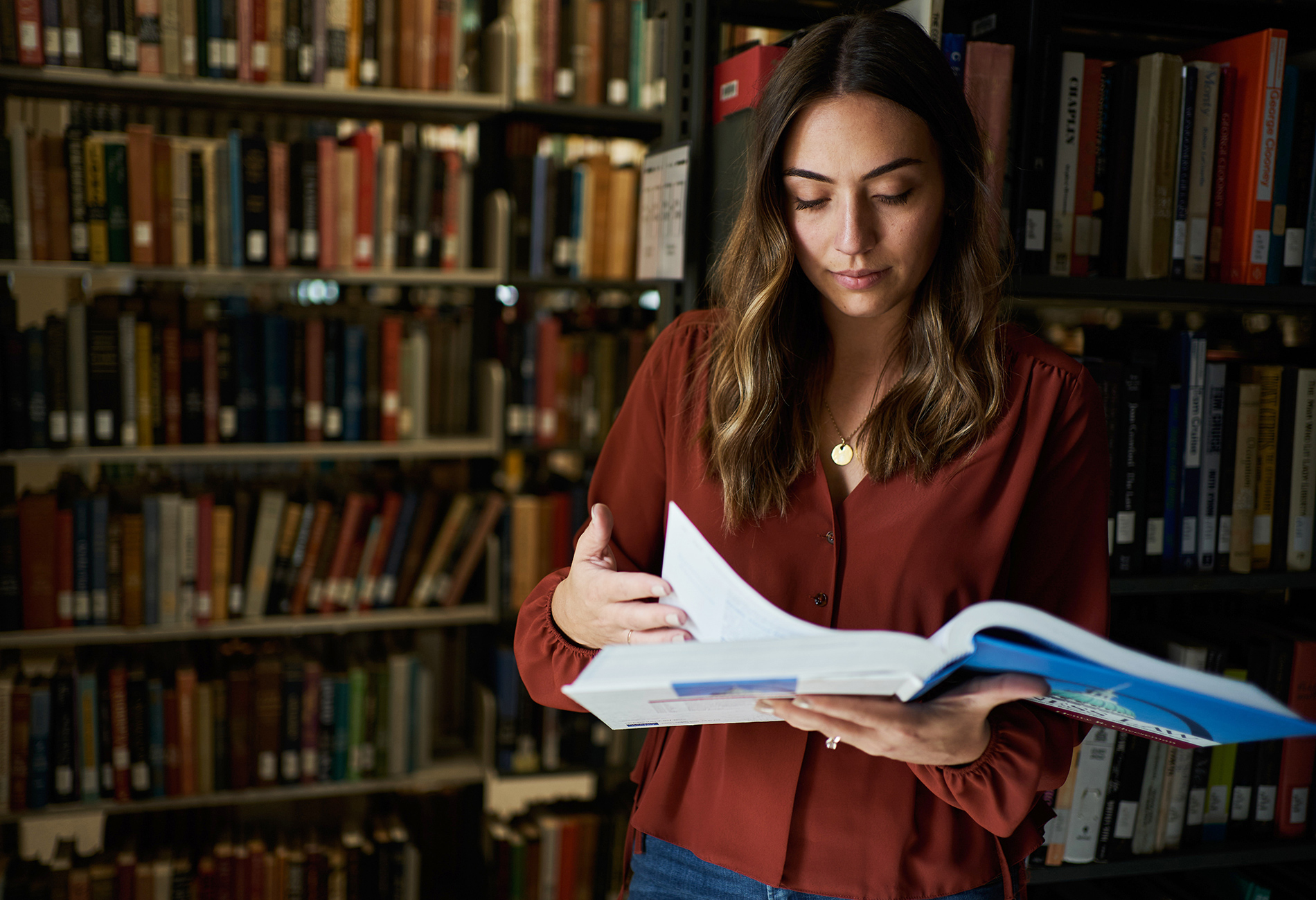 A female student reads a book while standing in the library