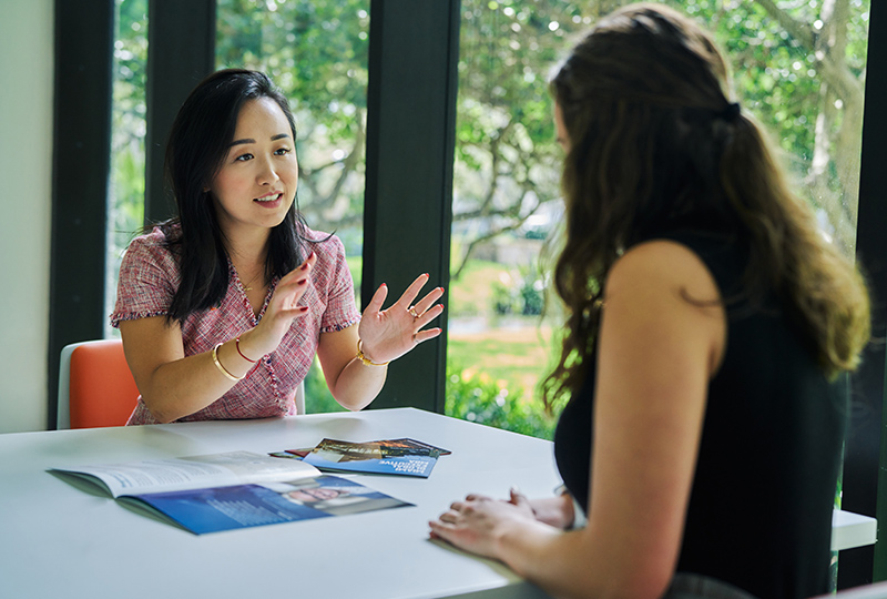 Two female students sit inside discussing programs