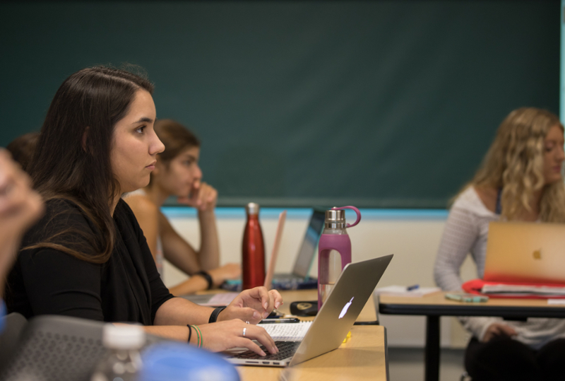Female student in a classroom in front of a laptop.