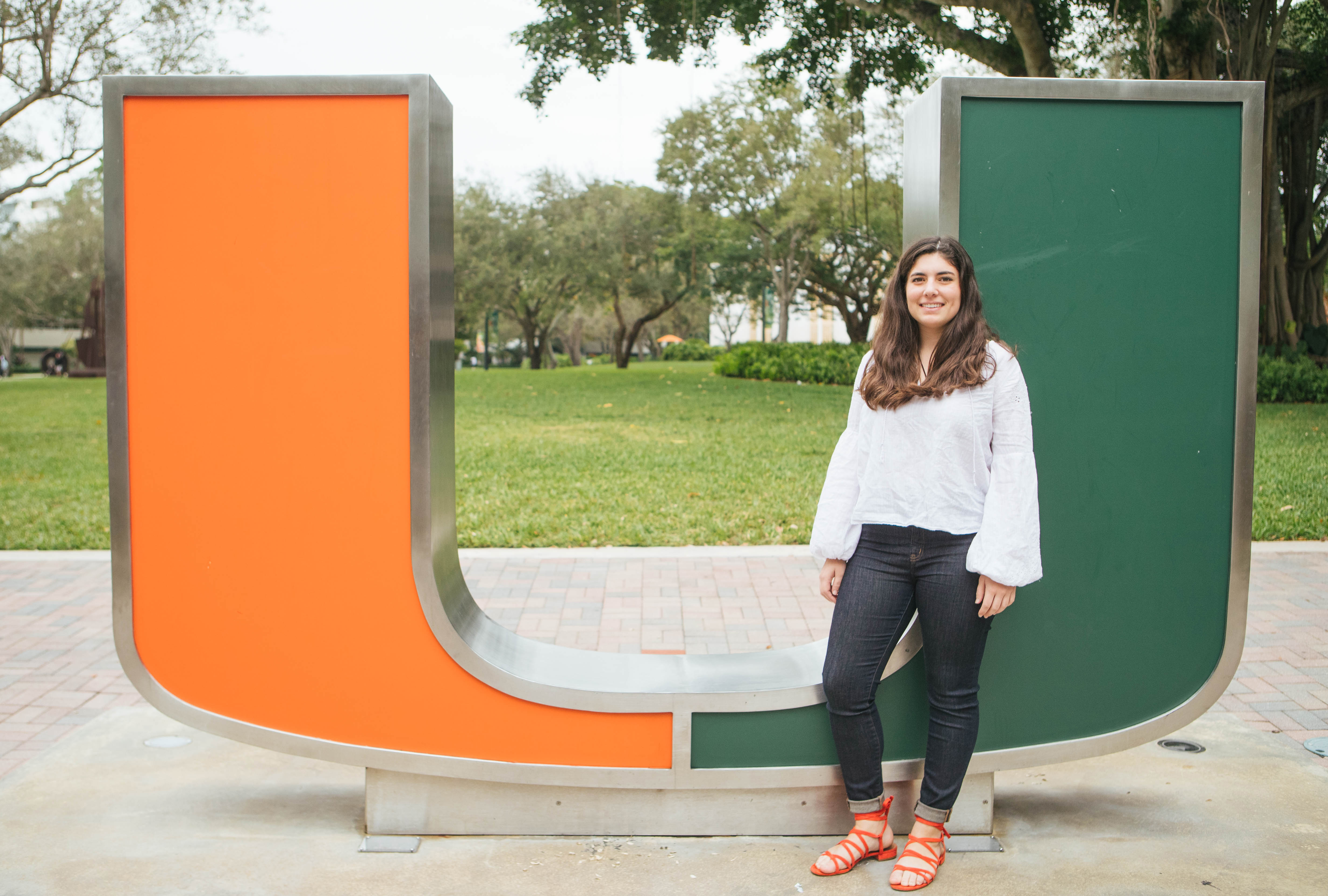 Student standing in front of a statue of the "U" Miami logo.