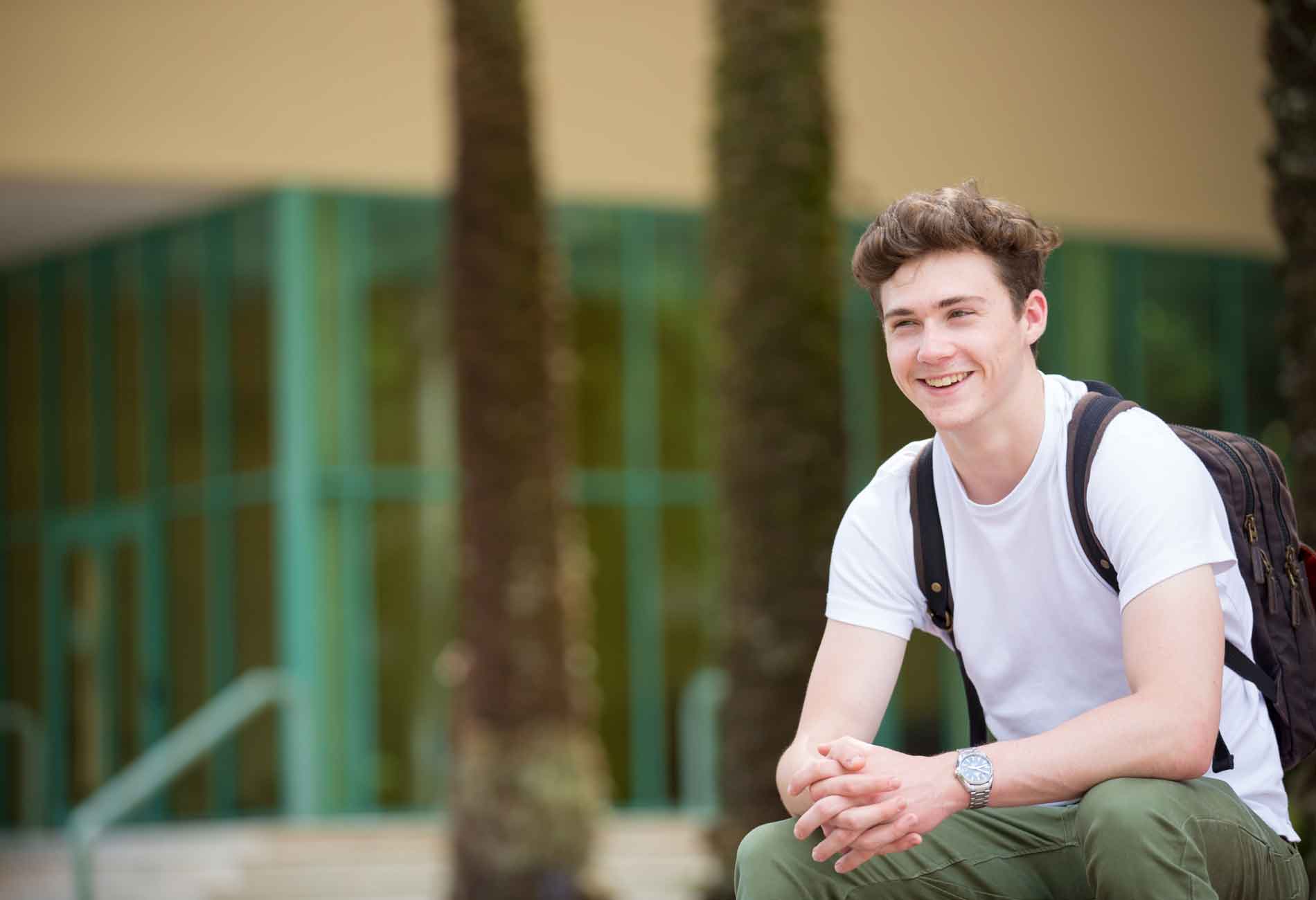 Student standing outside Miami Herbert Business School, palm trees in the background.