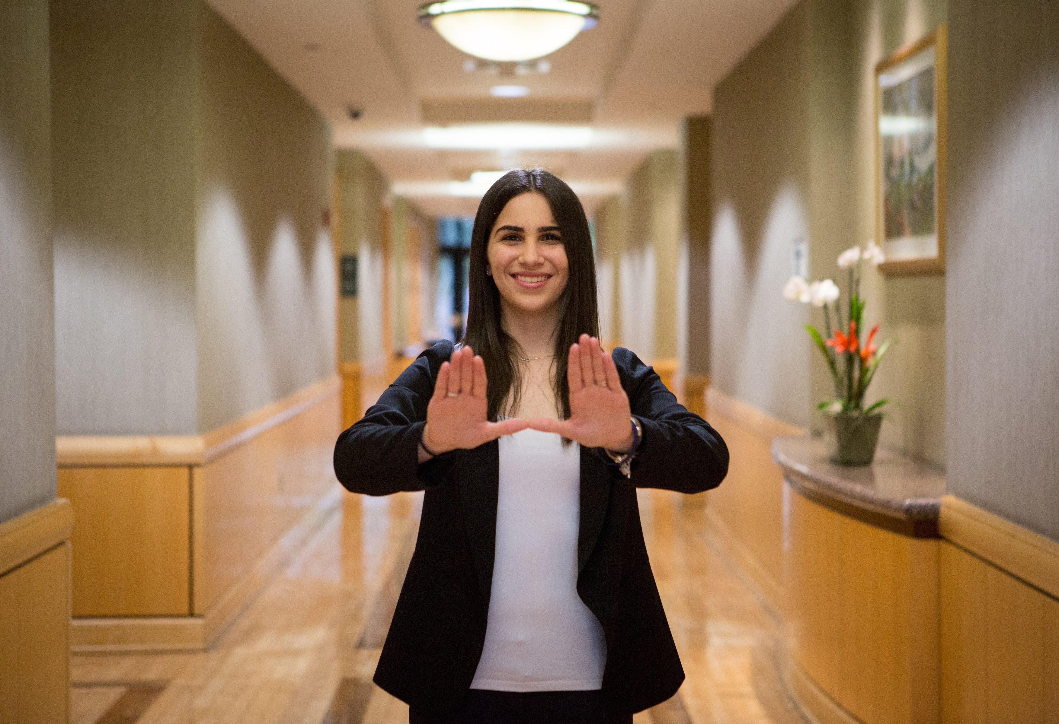 Female student inside the business school building holding up the U sign.