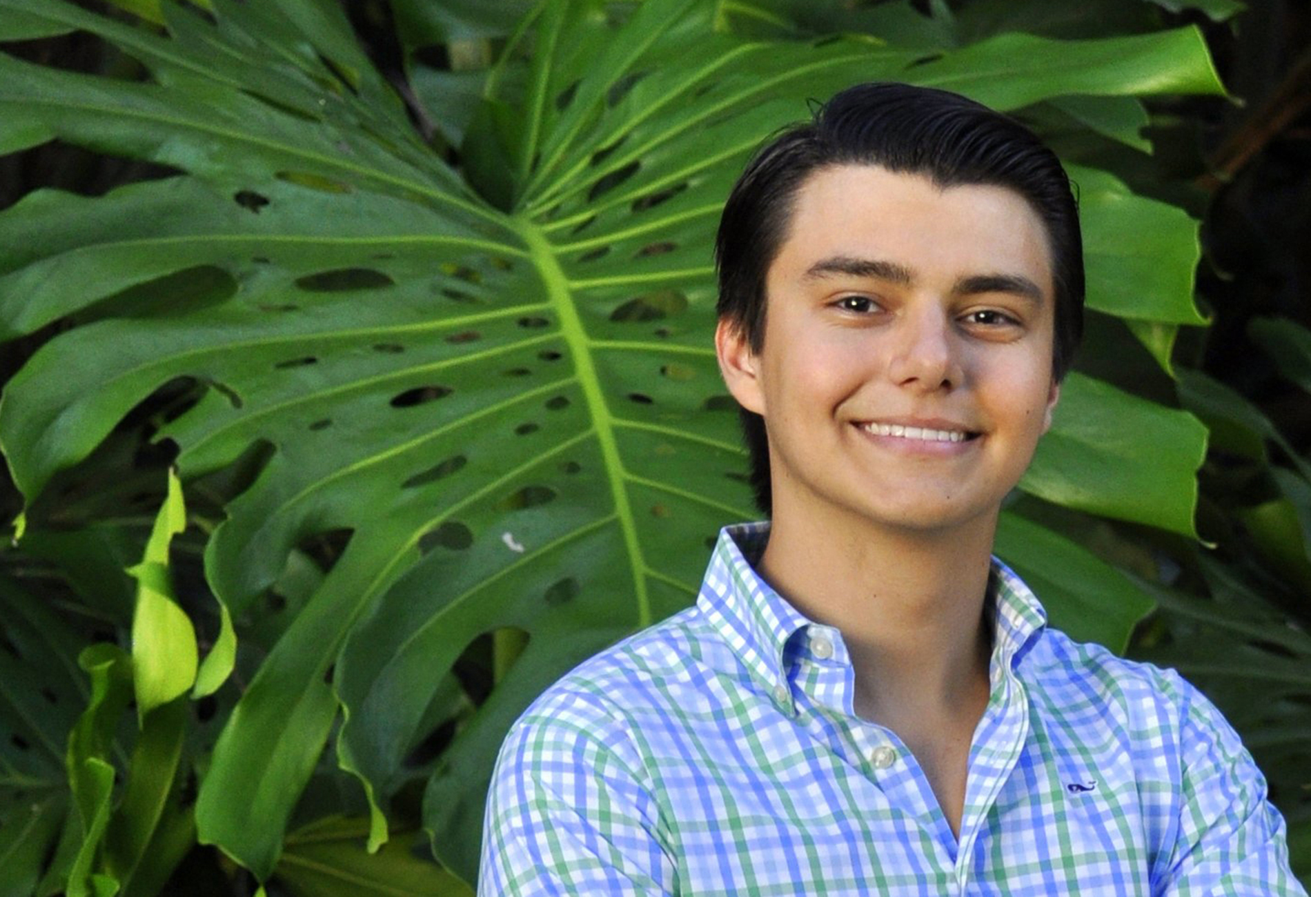 Male student standing outdoors with a monstera plant behind him.