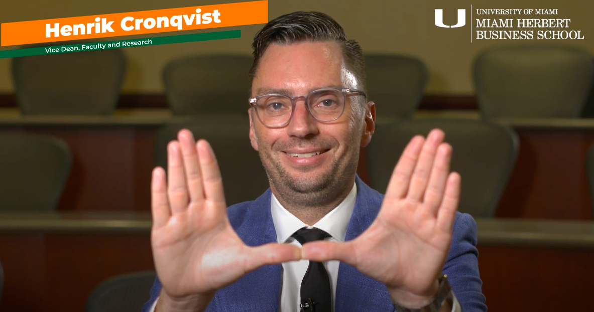Henrik Cronqvist holds his hands in a "U" shape while seated in an auditorium.