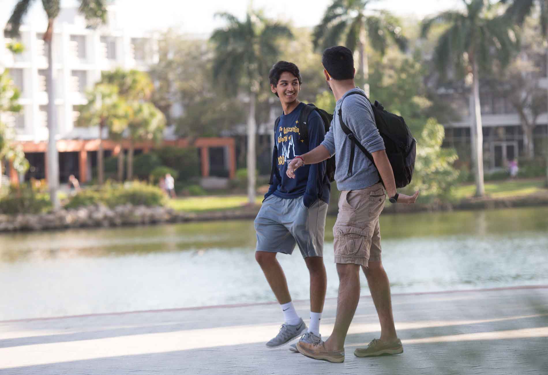 Students walking alongside the lake on the University of Miami Campus, palm trees in the background.