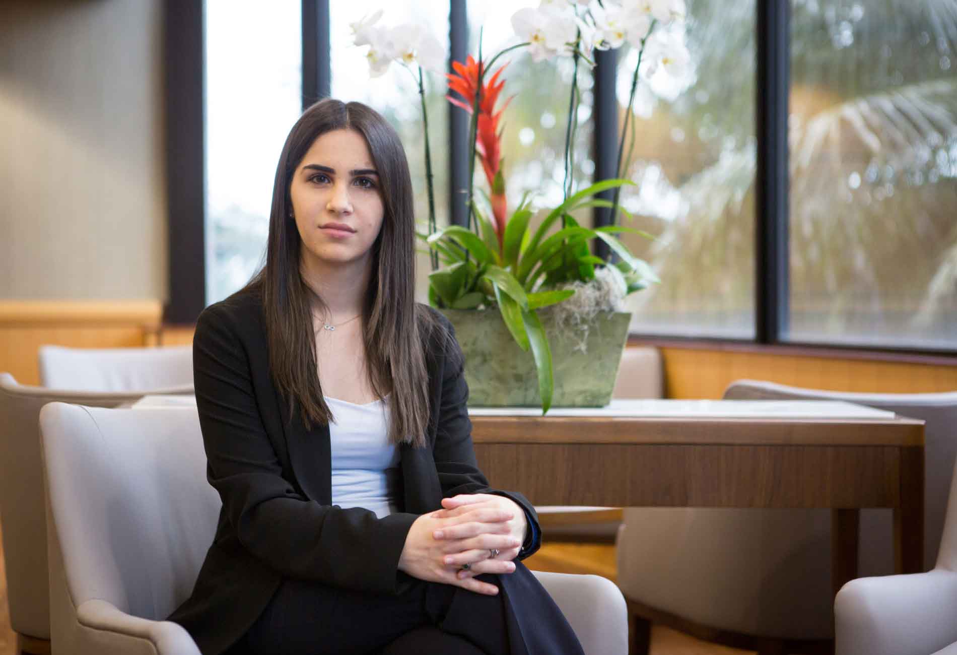 Female student sitting indoors, plant behind her.