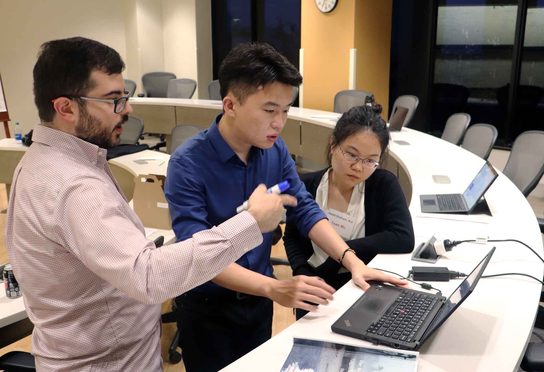 Students inside a classroom collaborating on a project via a laptop.