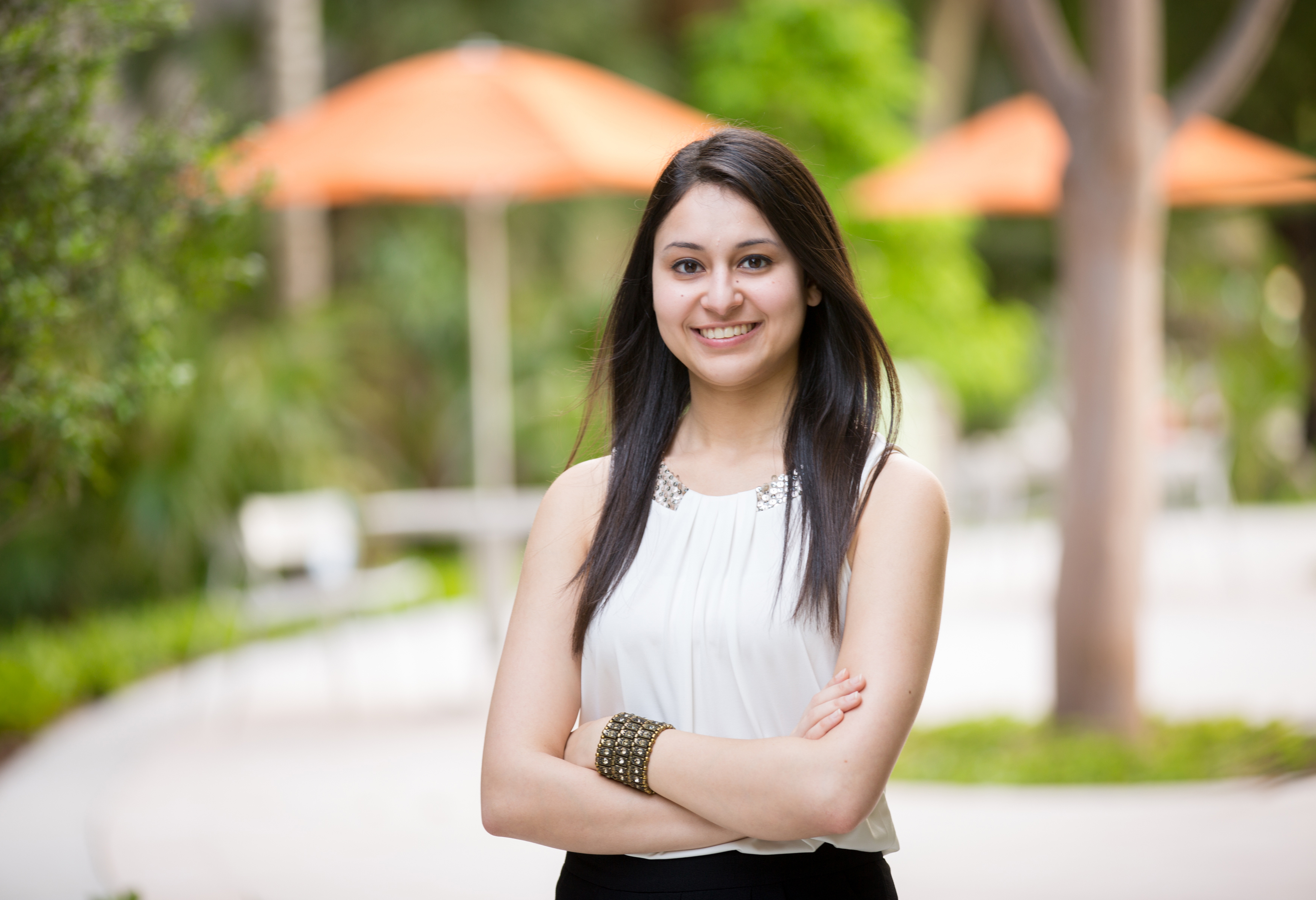 Close up of female student standing outside, orange umbrellas in the background.