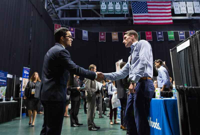 Two individuals in formal business attire shake hands.