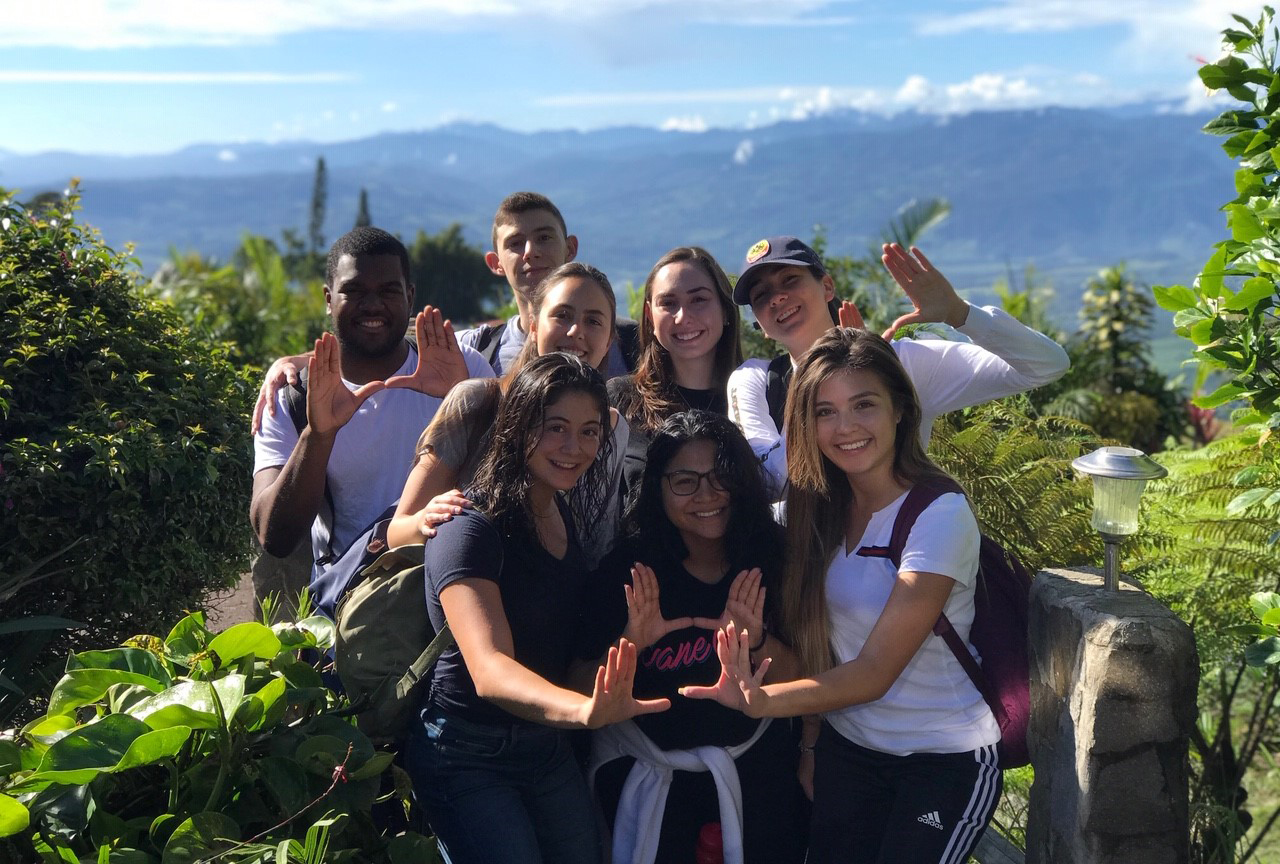 A group of students pose for a photo and hold their hands up in a "U" shape.