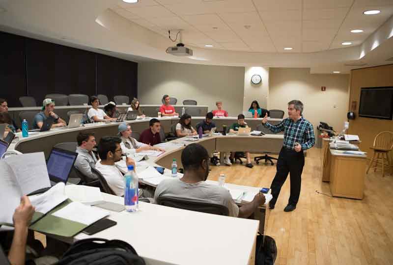 A professor gives a lecture to seated students.